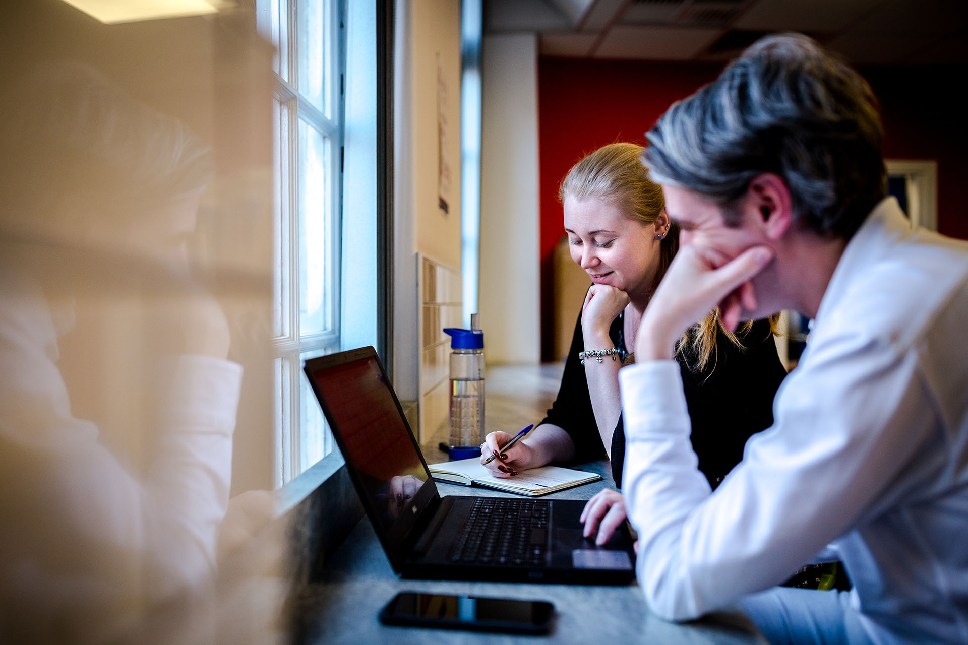 image of two active win employees sat by a window looking at a laptop